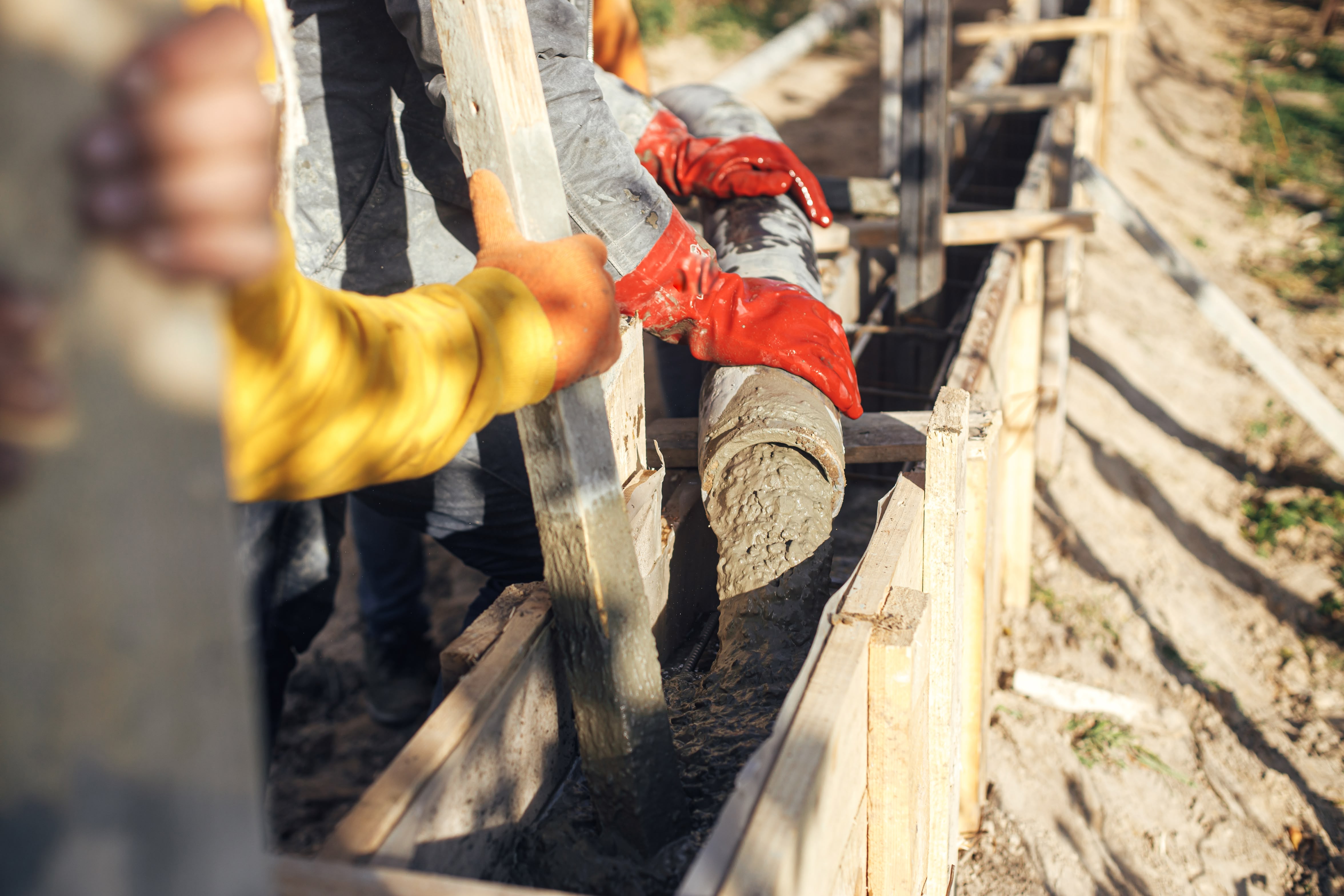 Construction workers pouring concrete into foundation formwork