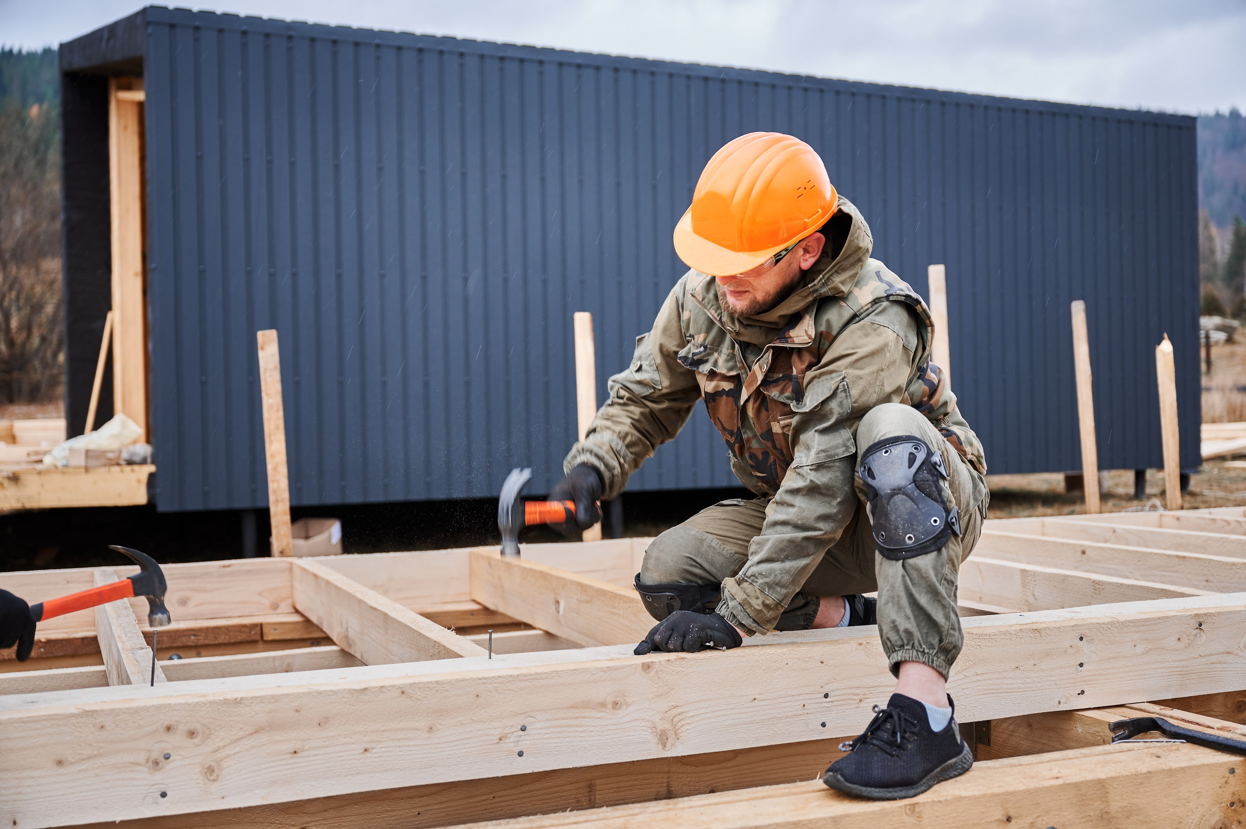 Worker in hard hat hammering wooden frame on construction site